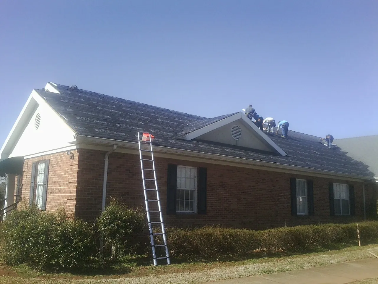 Crew tearing shingles off a brick ranch roof with a ladder set — Metal Roof Repair work by our crew in Sartell