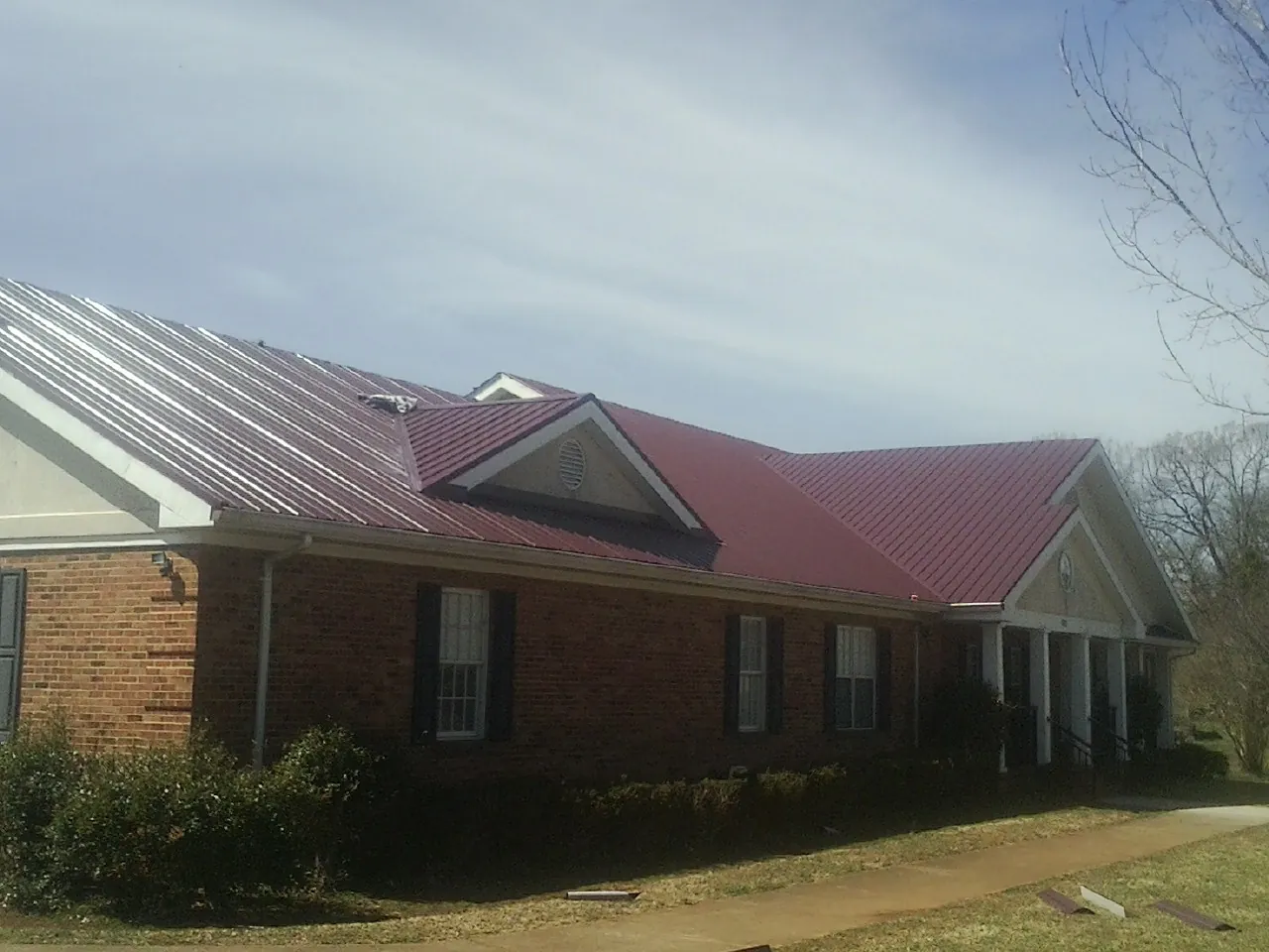 Red metal roof with gabled entries on a long brick building, from a Hail Damage Roof Repair job in Sartell