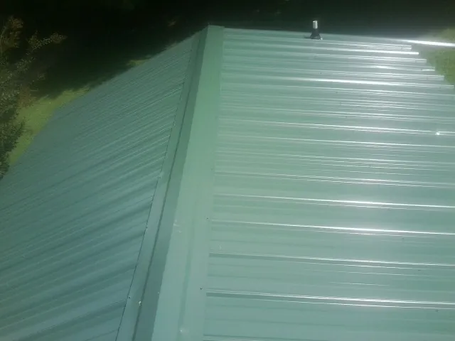 New green metal panels meeting at the ridge of a roof — Flat Roof Repair work by our crew in Sartell