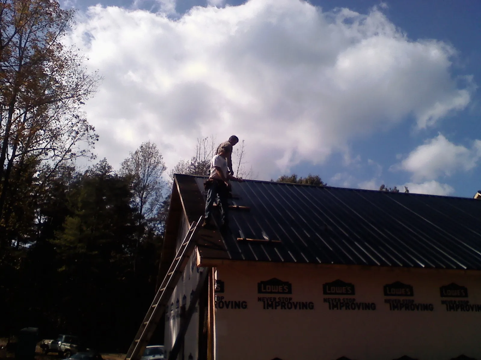 Roofer fastening dark metal panels high against a cloudy sky, from a Roof Inspection job in Sartell