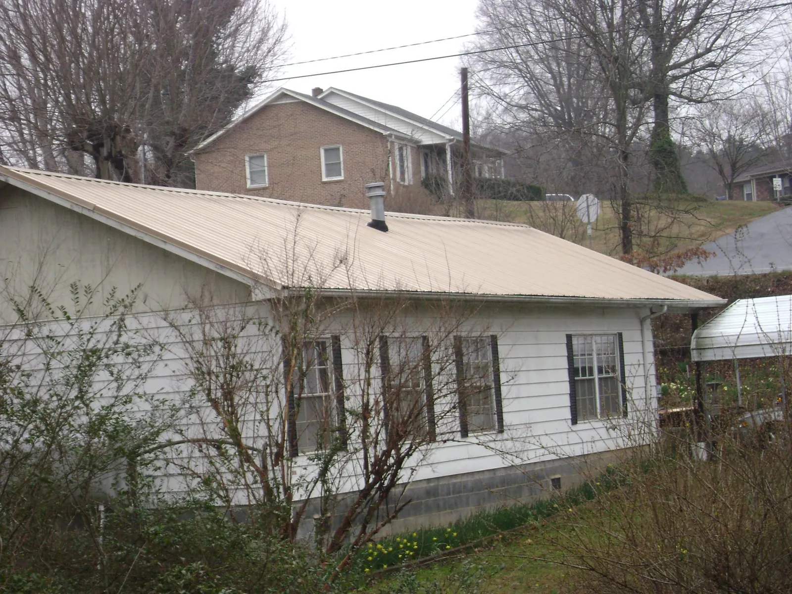 Tan metal roof on a white sided house set into a hillside — Commercial Roofing by Roofing Brothers in Sartell