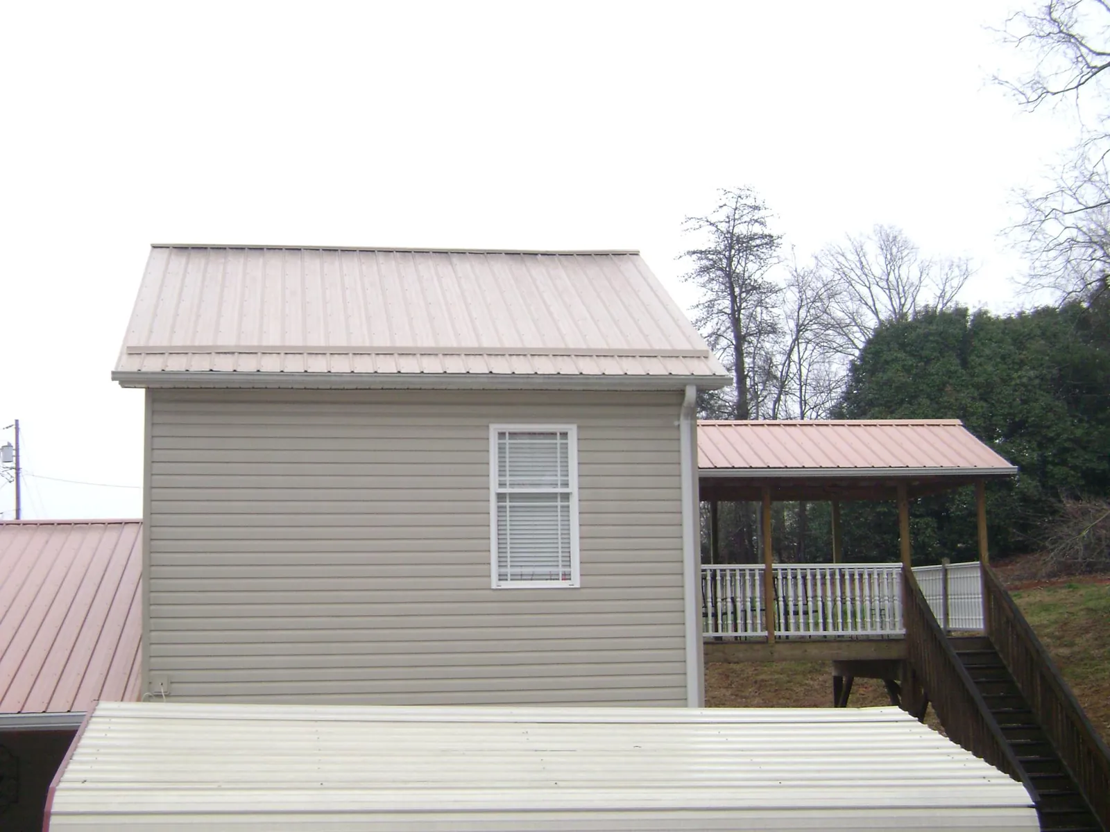 Tan metal roofs on a two story addition and attached porch, from a Roof Replacement job in Sartell
